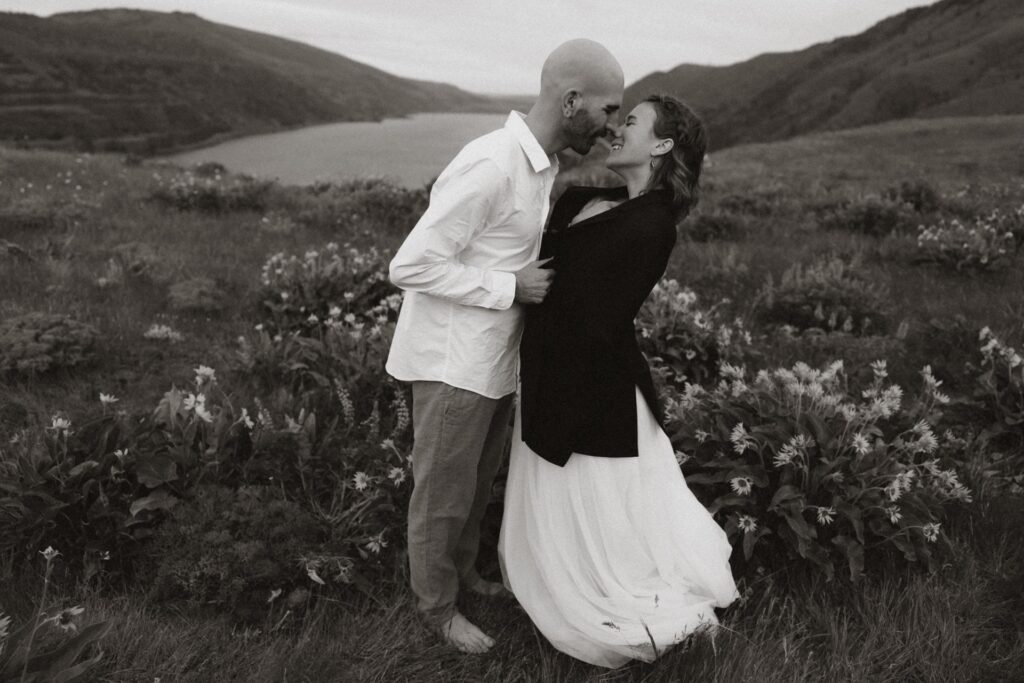 A bridal portrait of groom leaning into bride wearing coat jacket in wildflower field at Rowena Crest Viewpoint near Oregon