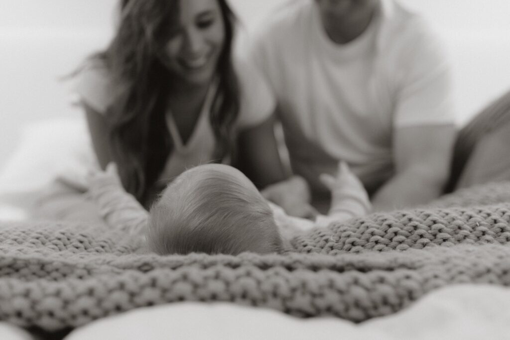 A family photo of a male and female staring at their baby on their bed