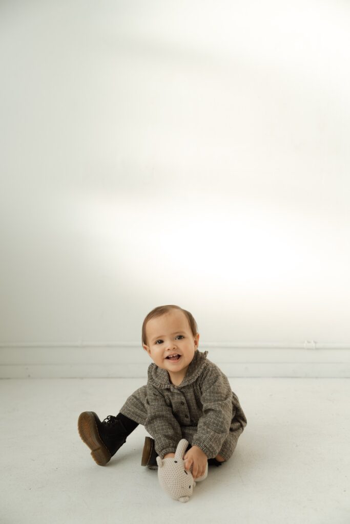 A kids portrait of a baby in gray dress wearing Dr. Marten boots smiling at camera at Northlight Studio near Seattle, WA