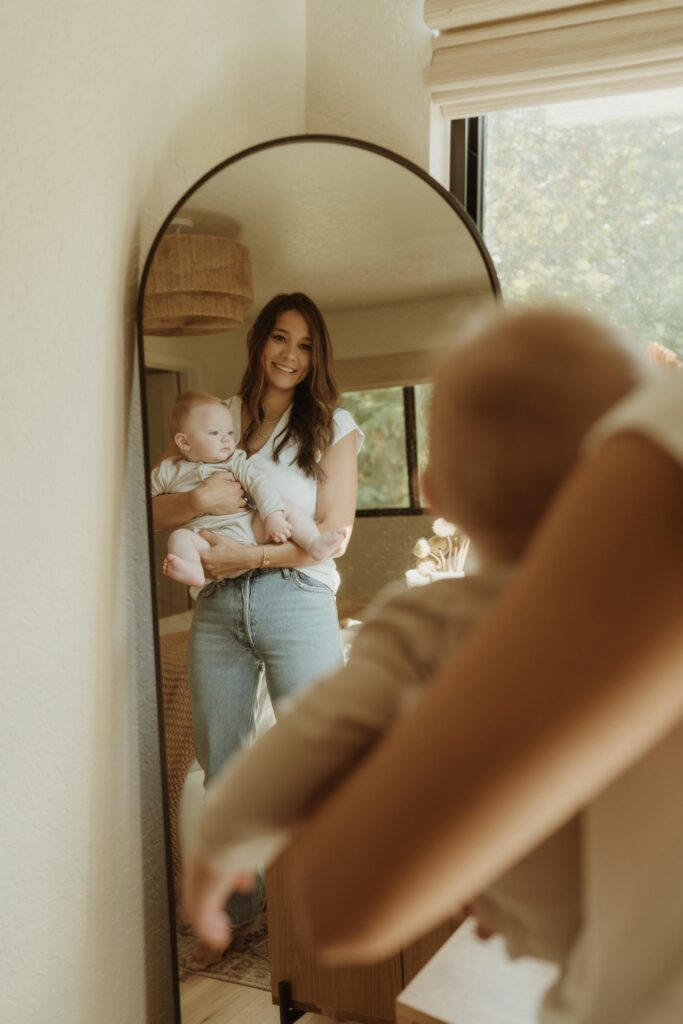 A motherhood photo of a female holding baby looking in mirror
