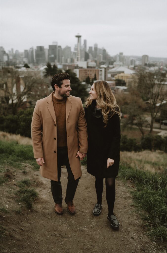 A couples portrait of a male and female walking together wearing coats at Kerry Park near Seattle, WA