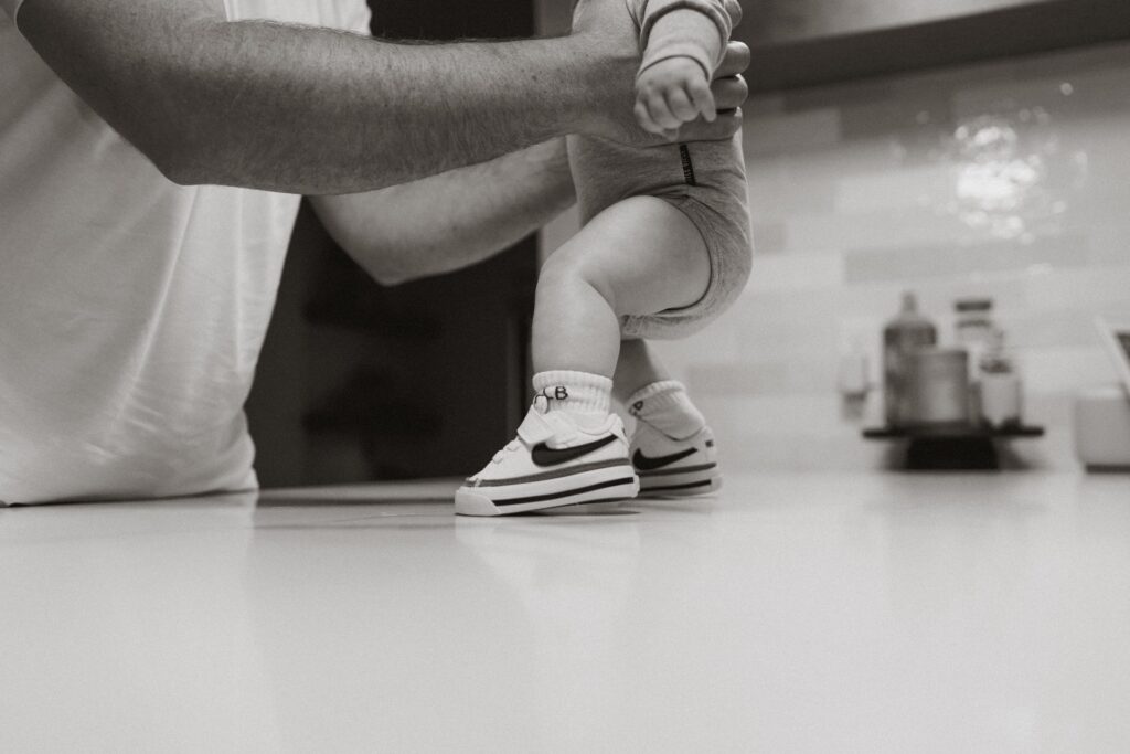 A baby closeup photo of a male holding baby on counter wearing sneakers