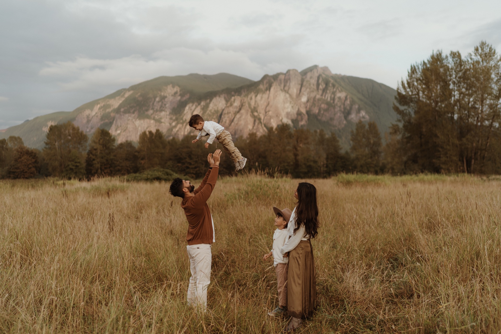 A family portrait of a Father throwing up little boy with Mother and son standing beside them in field at Mount Si near North Bend, WA