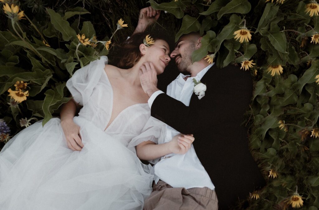 A bridal portrait of a wedding couple laying in green grass surrounded by sunflowers at Rowena Crest Viewpoint near Hood River, OR