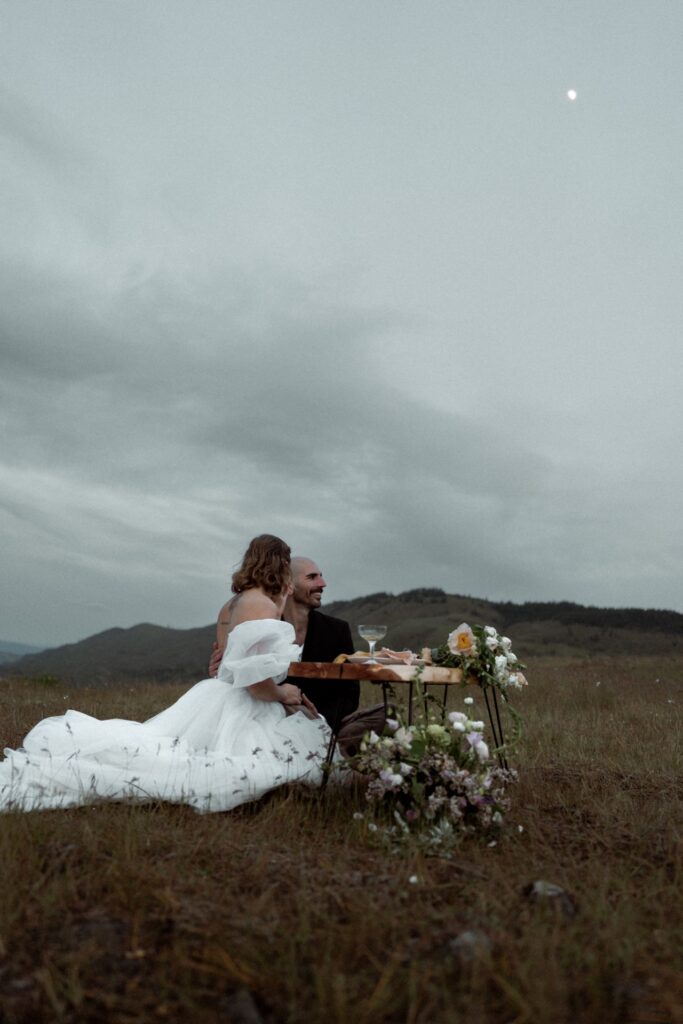 A male and female bridal couple sitting in field at Rowena Crest Viewpoint with low table.