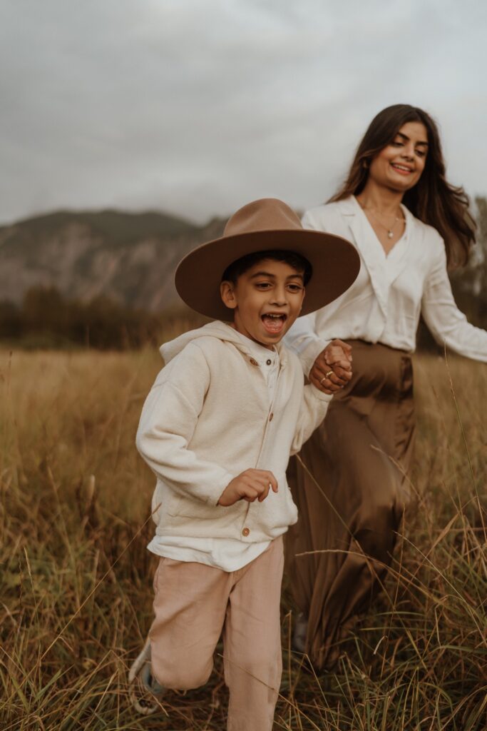 A family portrait of a female running in field with son wearing brown hat at Mount Si near North Bend, WA