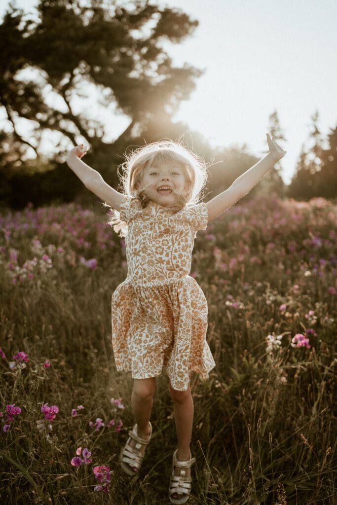 A children's portrait of a little girl wearing floral dress jumping in field at Discovery Park near Seattle, WA