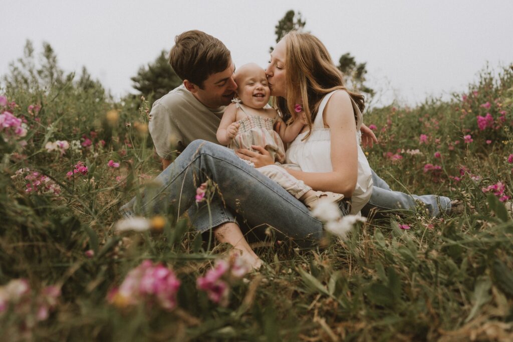 Family sitting in wildflower field kissing baby Discovery Park