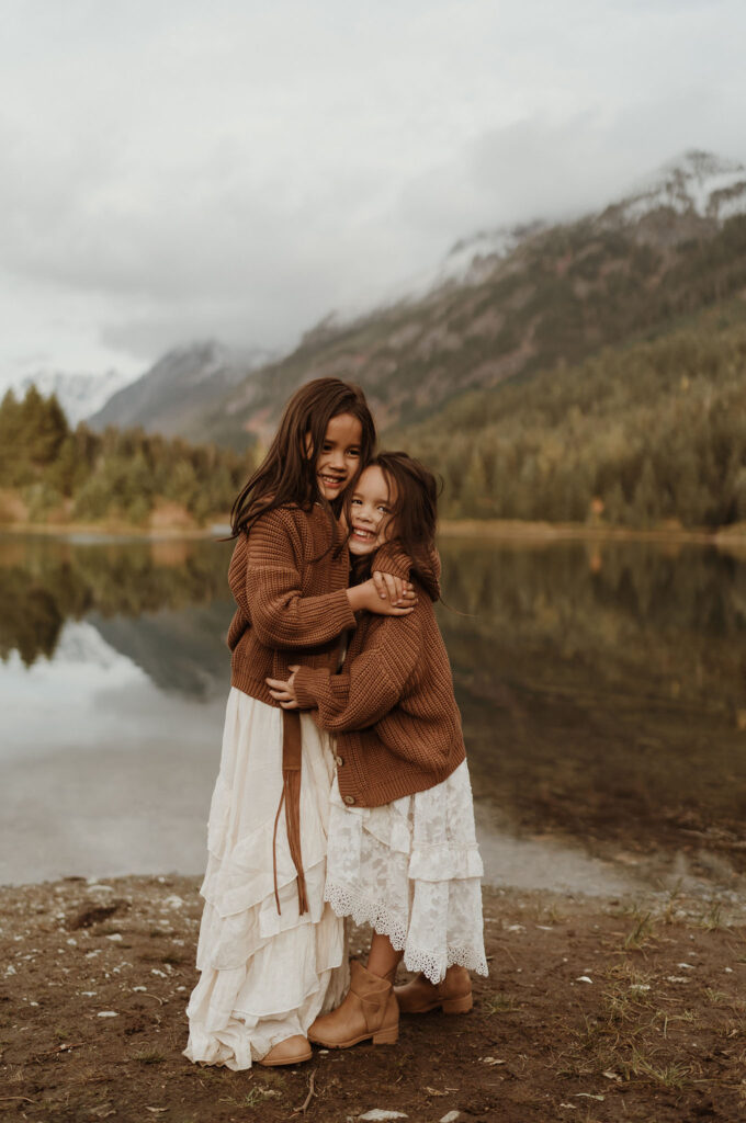 A children's portrait of two little girls wearing brown sweaters hugging at Gold Creek Pond near Snoqualmie Pass, Seattle, WA.