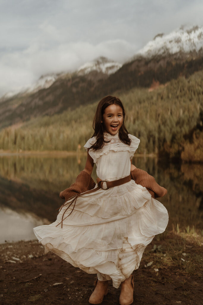 A children's portrait of a little girl wearing white dress playing with skirt at Gold Creek Pond near Snoqualmie Pass, Seattle, WA.