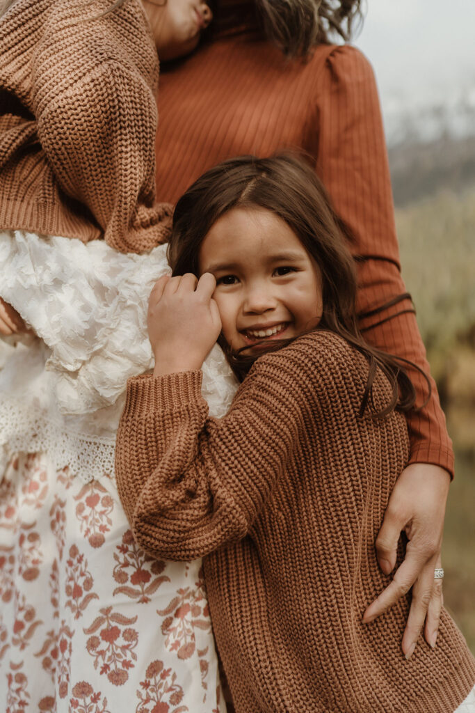 A children's portrait of a little girl wearing a brown sweater snuggling with female at Gold Creek Pond near Snoqualmie Pass, Seattle, WA.
