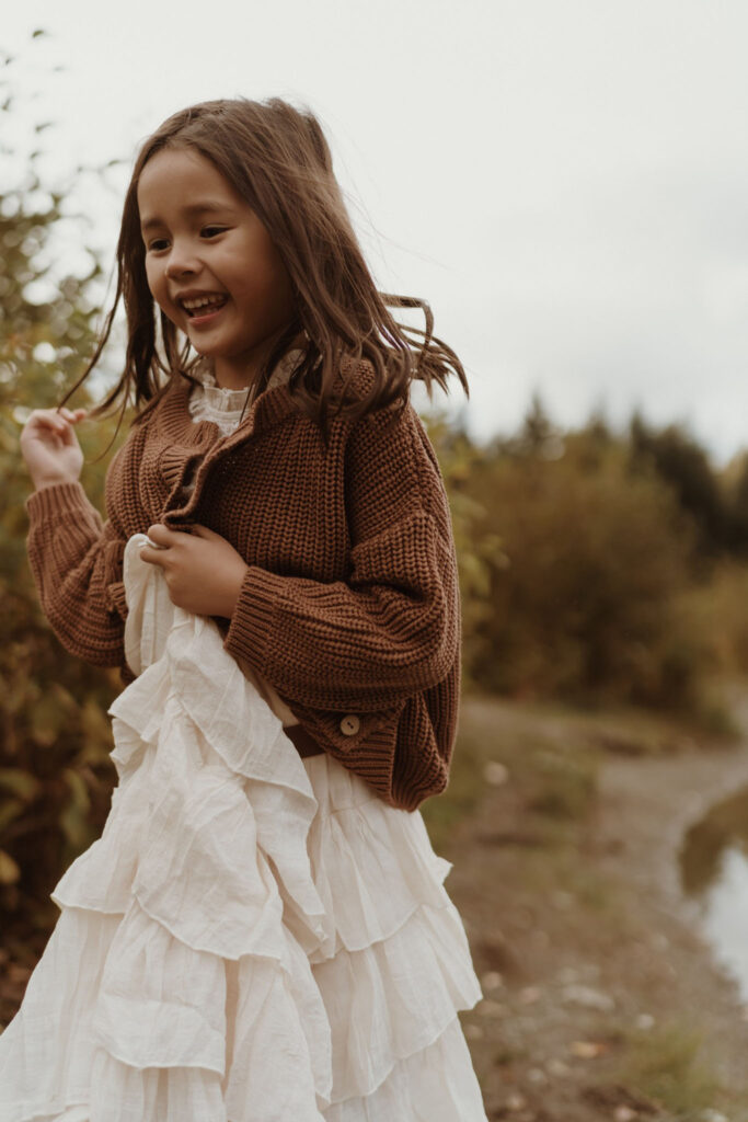 A children's portrait of a little girl wearing a brown sweater running at Gold Creek Pond near Snoqualmie Pass, Seattle, WA.