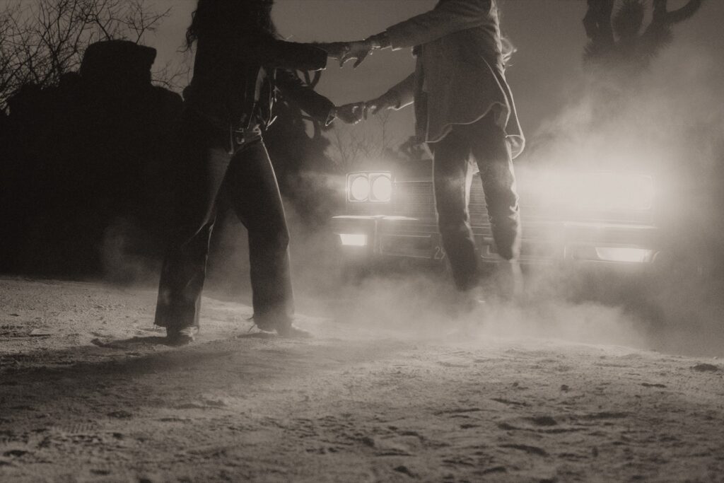 Two females dancing in front of car headlights in Joshua Tree National Park.