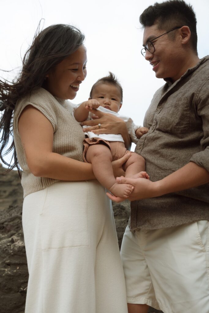 A family photo of male and female holding newborn baby at secluded beach cove in Oahu, Hawaii.
