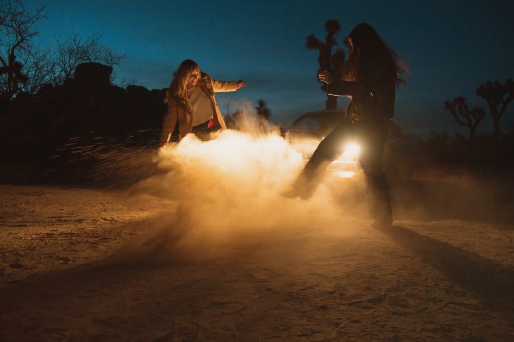 Two females kicking dirt in front of car headlights in Joshua Tree National Park.