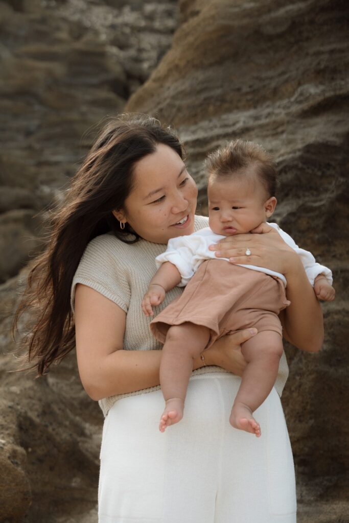 A portrait of a female holding newborn baby at beach rock canyon near Oahu, Hawaii.