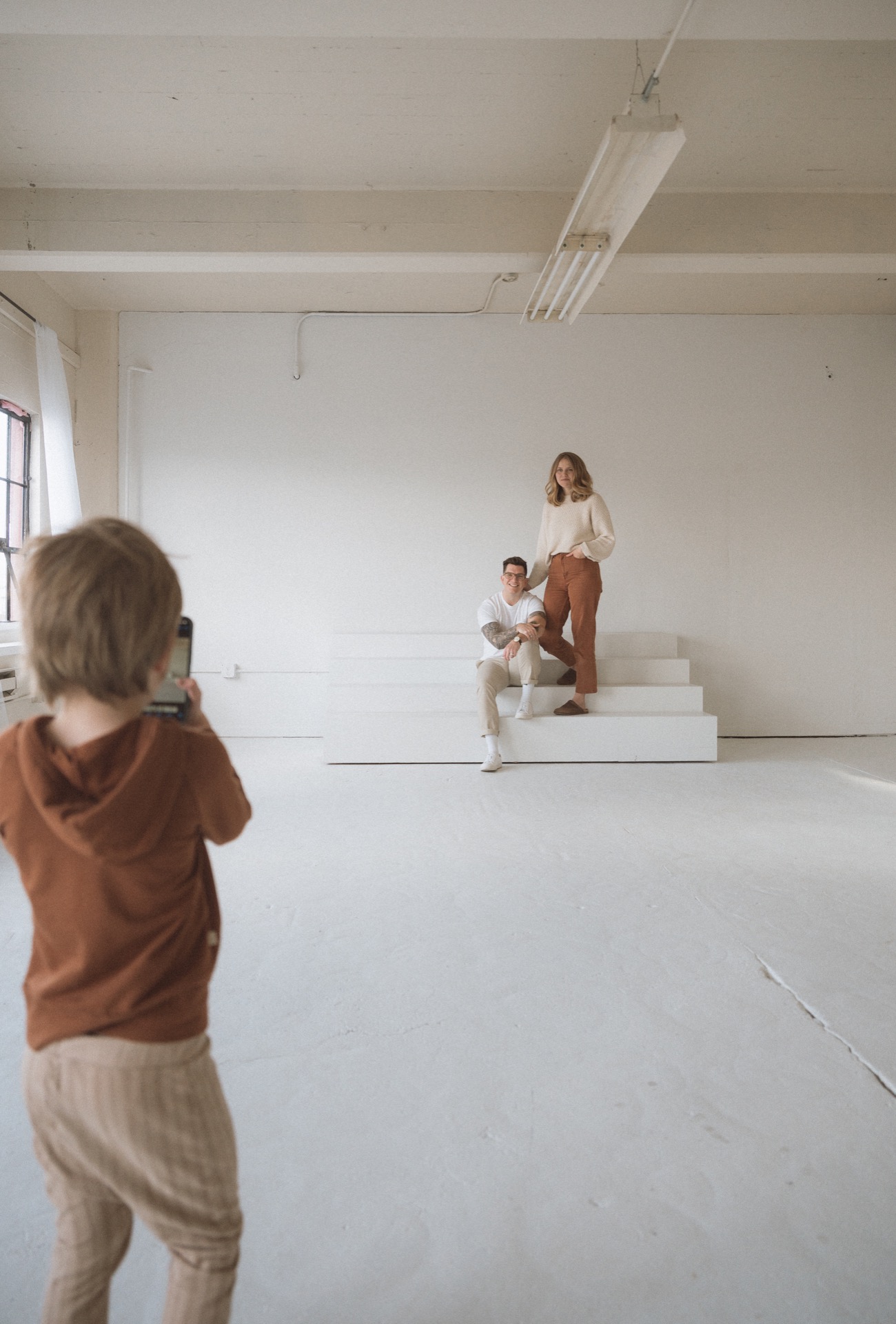 Little boy taking photo of male and female on white stairs in studio near Seattle, WA.