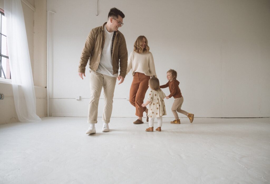 A family portrait of a male and female running around in circles with kids in all white studio near Seattle, WA.