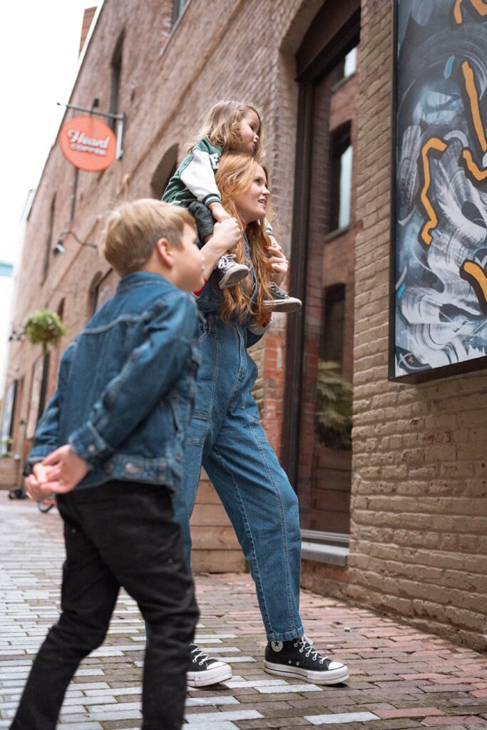 female looking at art with son on shoulders in pioneer square alley