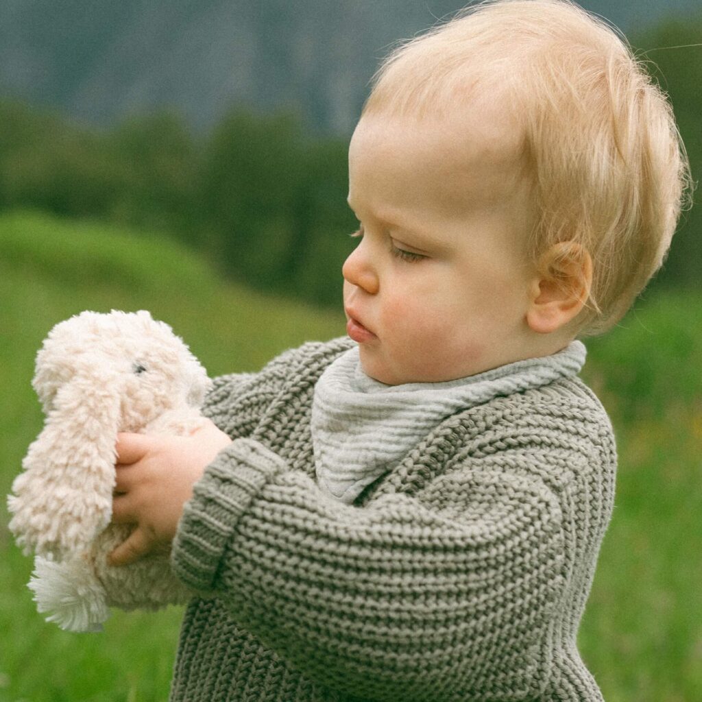 toddler holding bunny rabbit stuffie in field