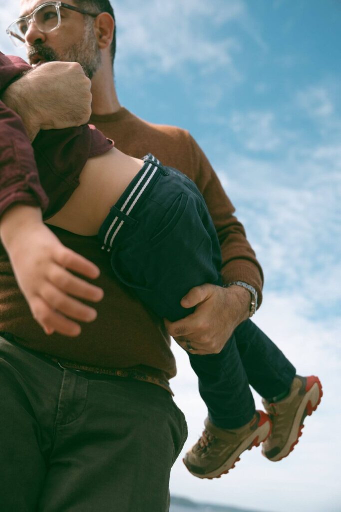 father carrying little boy at beach