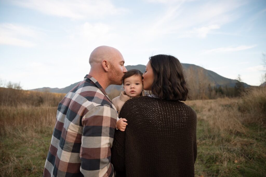 family kissing baby in field at mount si