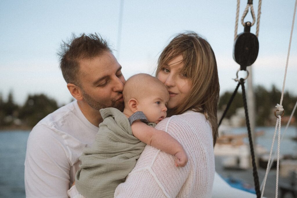 male and female holding swaddled newborn baby on boat near beach