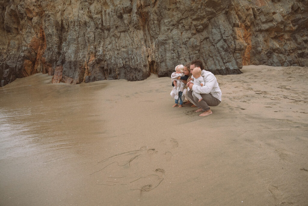 mother and father crouching near ocean with small children