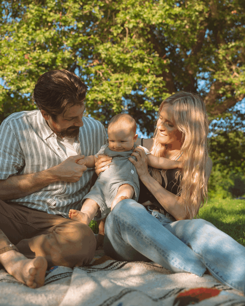 family of three with newborn baby in summer at park