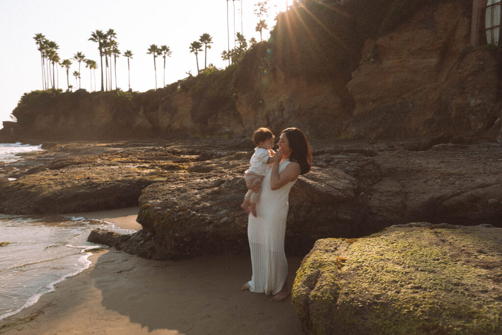 Mother holding her baby near the rocks at Shaw’s Cove during a newborn family sunset session.