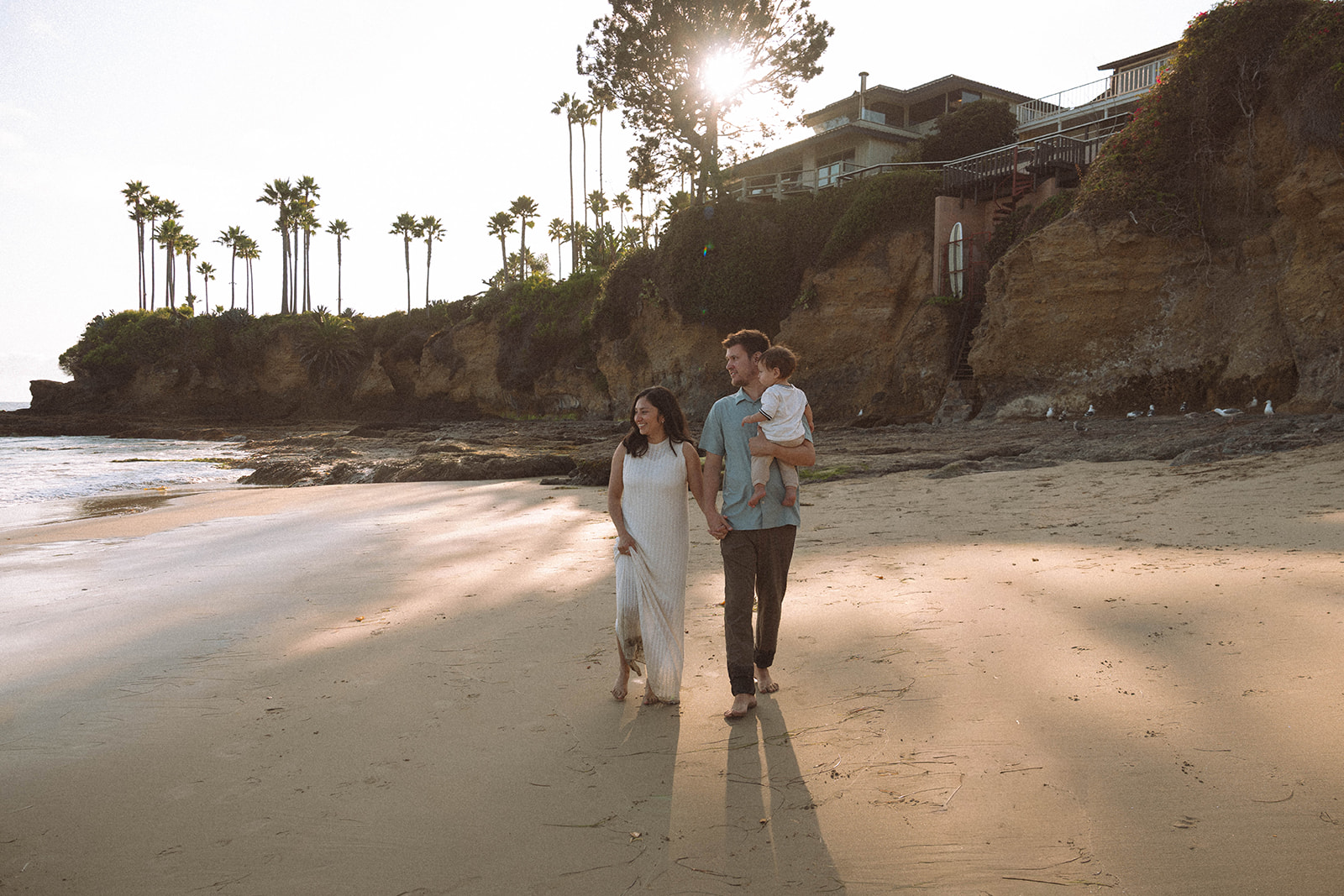 Parents walking hand in hand with their child along the beach in Laguna Beach at golden hour.