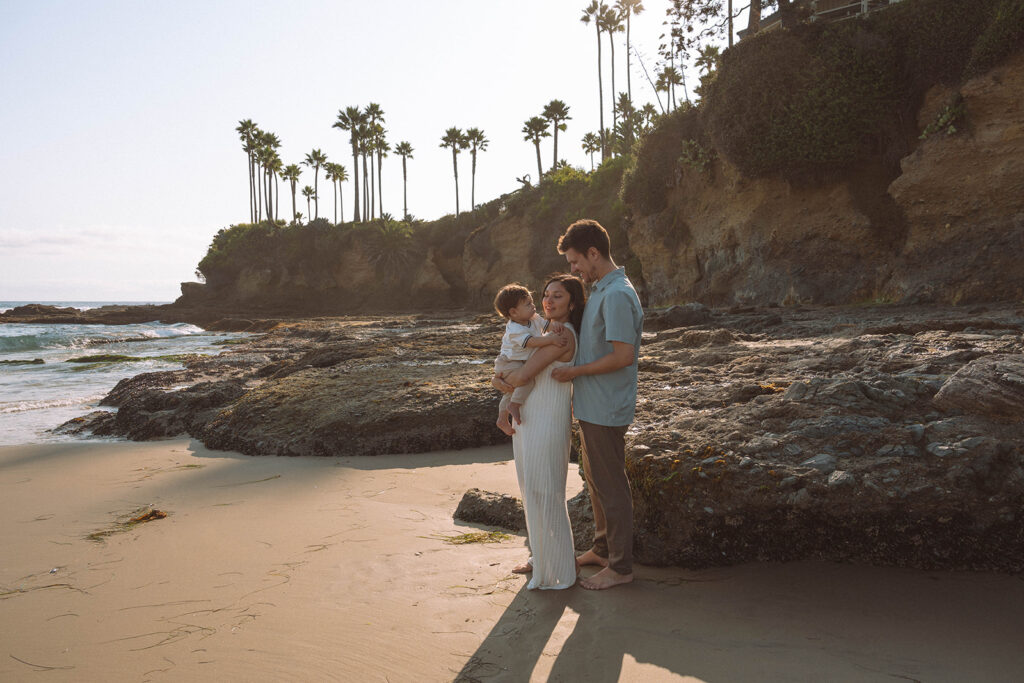 Family standing together near the rocks with palm trees in the background during a sunset photoshoot in Laguna Beach.