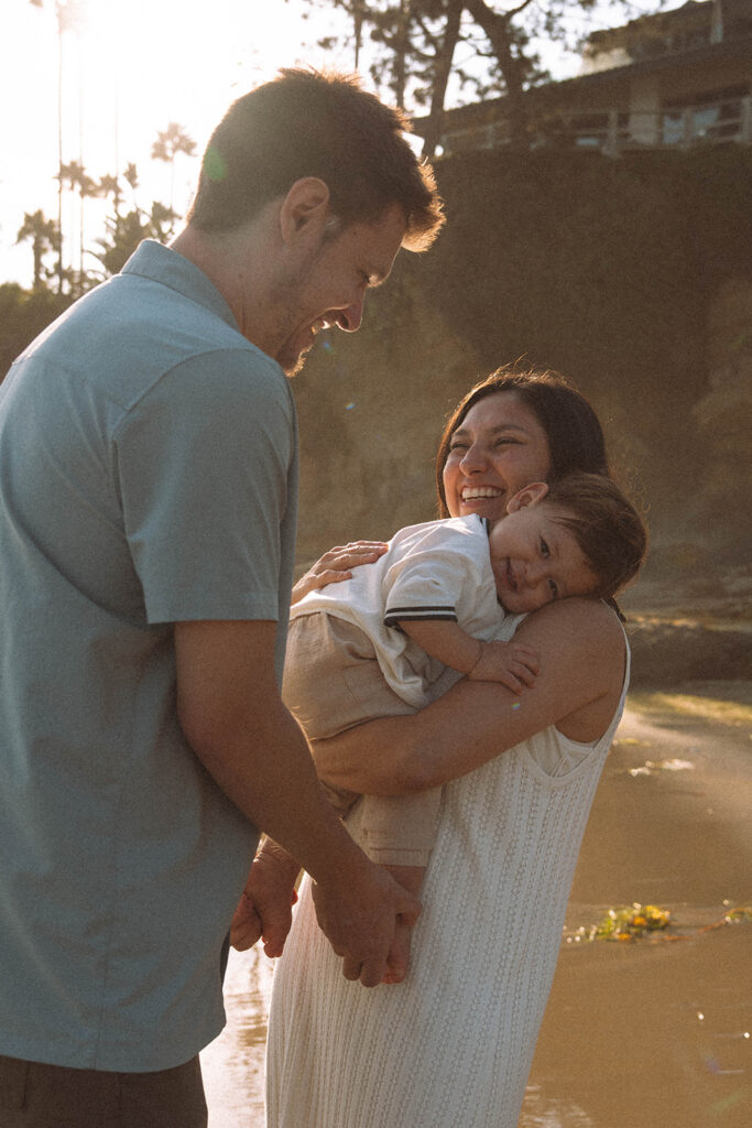 Parents smiling while holding their baby during a sunset family photoshoot in Laguna Beach.