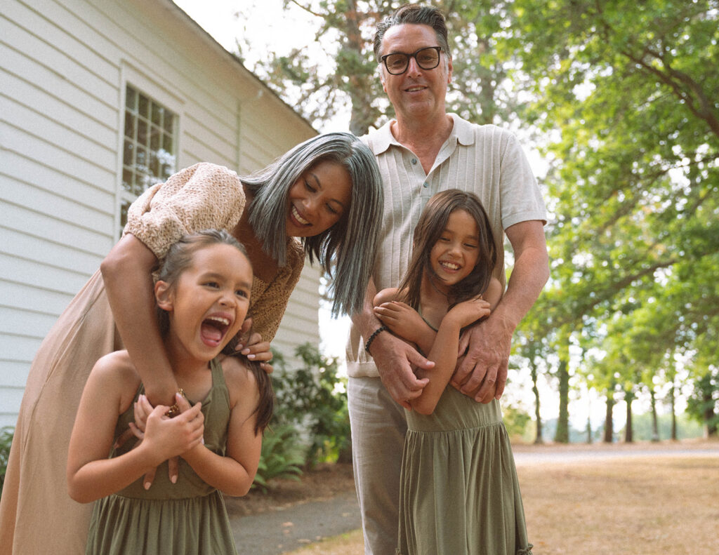 Family laughing together outside, with mom, dad, and two daughters during candid photos in Irvine, Orange County.
