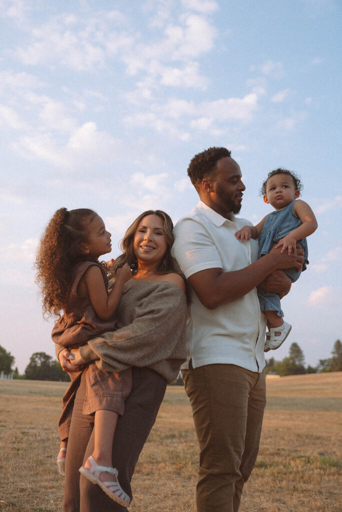 Family standing together in an open field with golden sky, styled in relaxed natural tones for sunset photography.