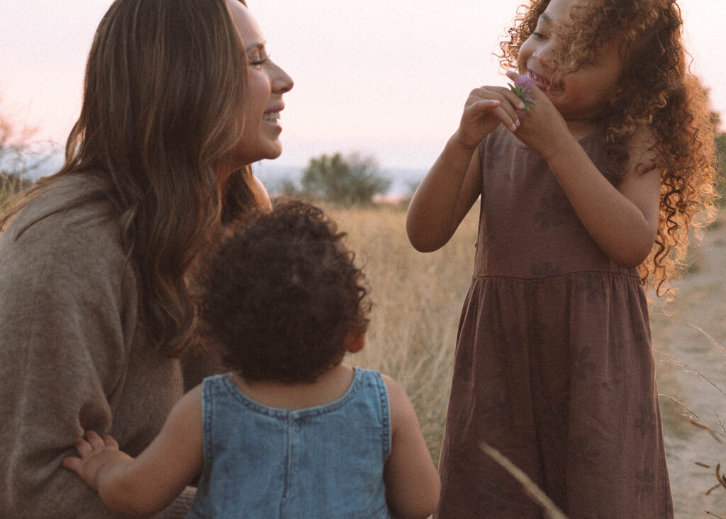 Mother and daughters in neutral and earthy outfits, smiling and playing together during golden hour family photos.