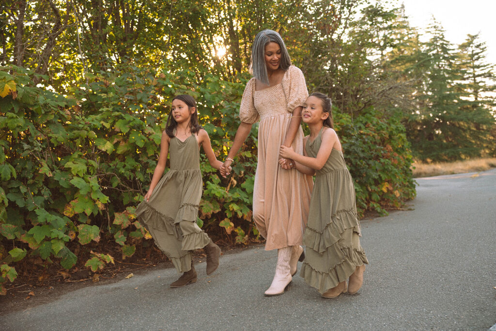 Mom walking with her daughters, holding hands and smiling in golden hour light during a fall family photography session.