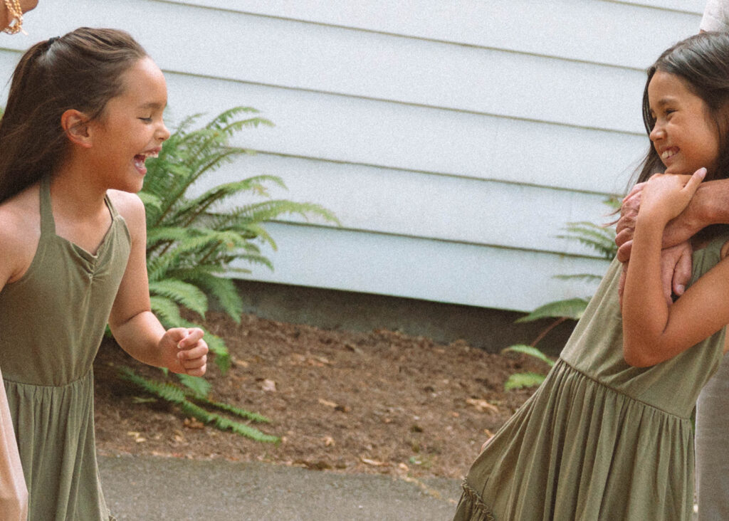 Two sisters in matching green dresses laughing together during family photos in Irvine, Orange County.
