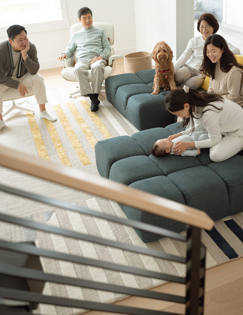Grandparents, parents, and newborn baby relaxing together in a modern living room during an Irvine in-home family session.