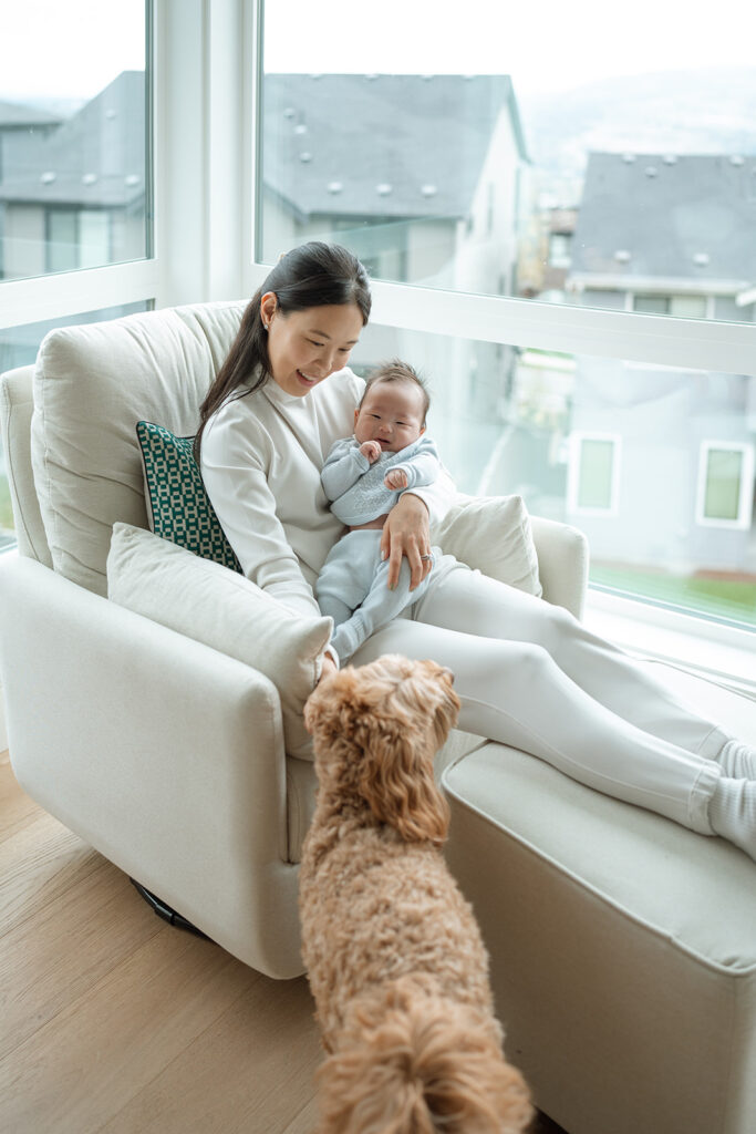 Mother cuddling newborn baby while the family dog greets them during lifestyle newborn photography at home in Orange County.