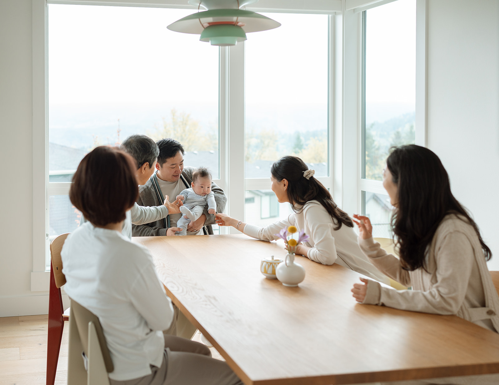 Family gathered around dining table with newborn baby at the center during candid in-home newborn photography in Orange County.