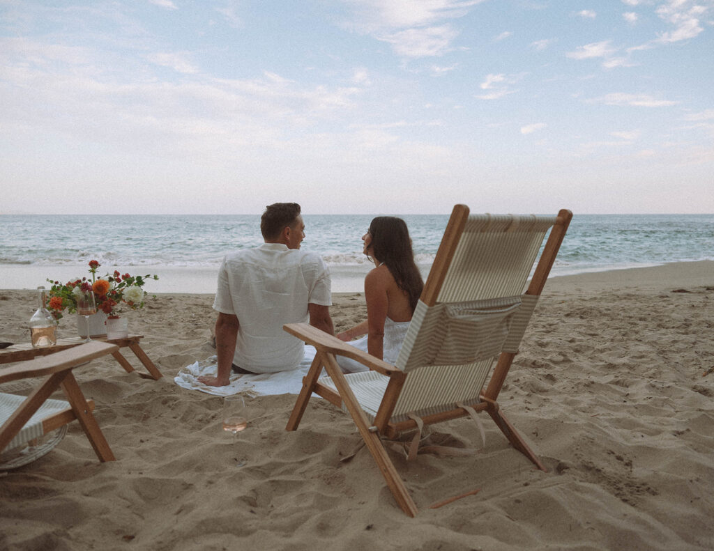 Couple relaxing during a beach picnic with flowers and chairs in Laguna Beach.