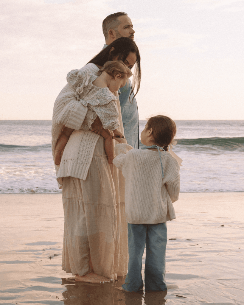 Family standing together on the shoreline with reflections in the wet sand, captured at sunset in Orange County.
