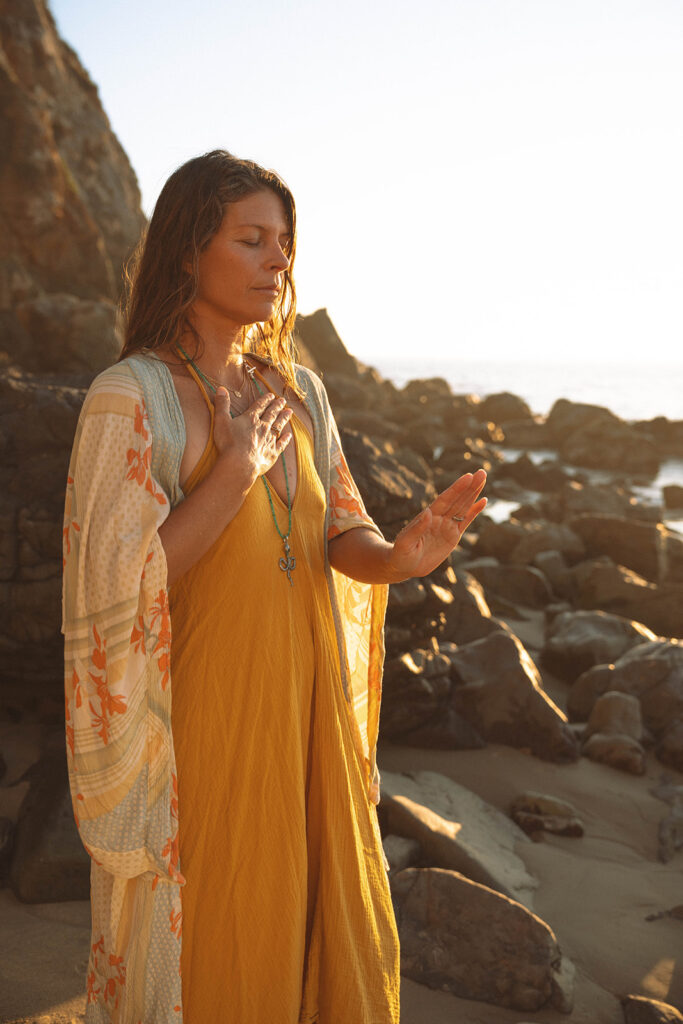 Mindful moment during Laguna Beach branding photos — a yoga business owner standing by the rocks at sunrise in soft, natural light.