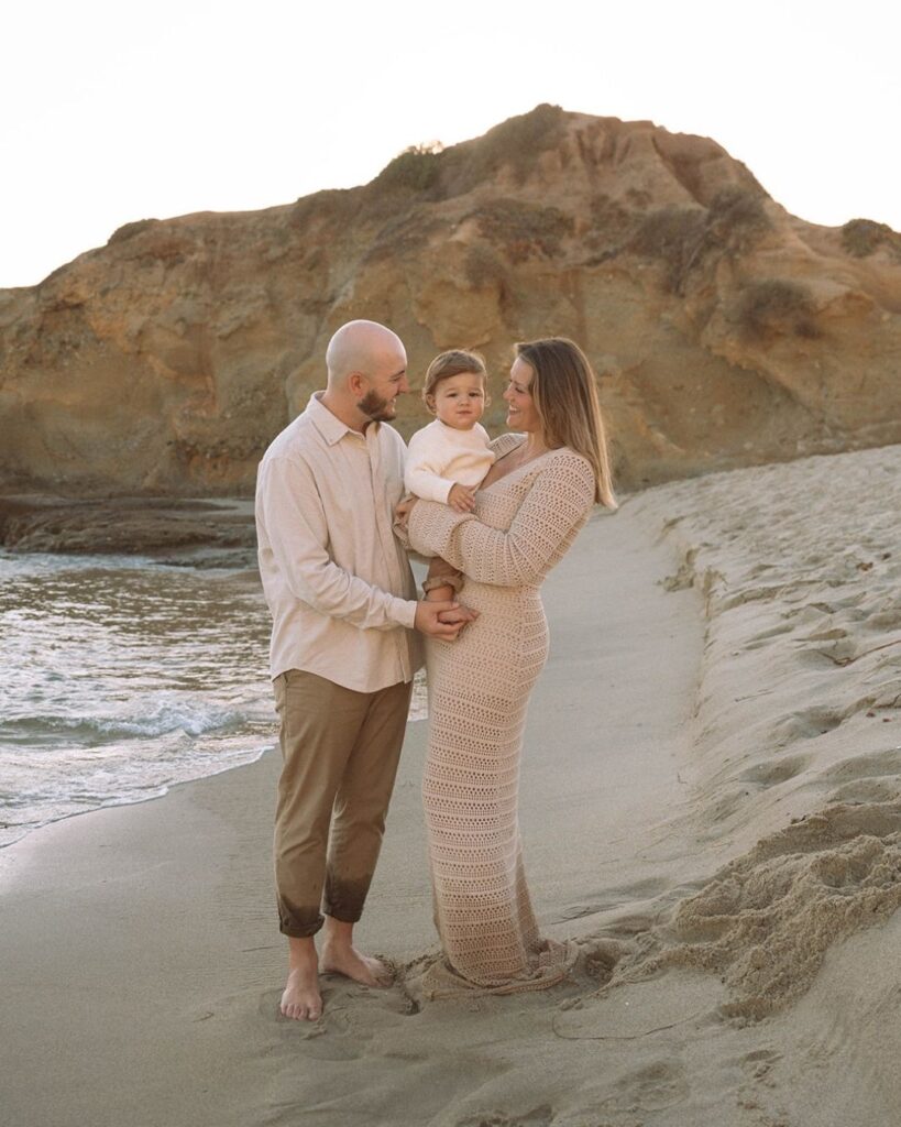 Family of three standing on the shoreline at Goff Cove Beach in Laguna Beach during sunset.