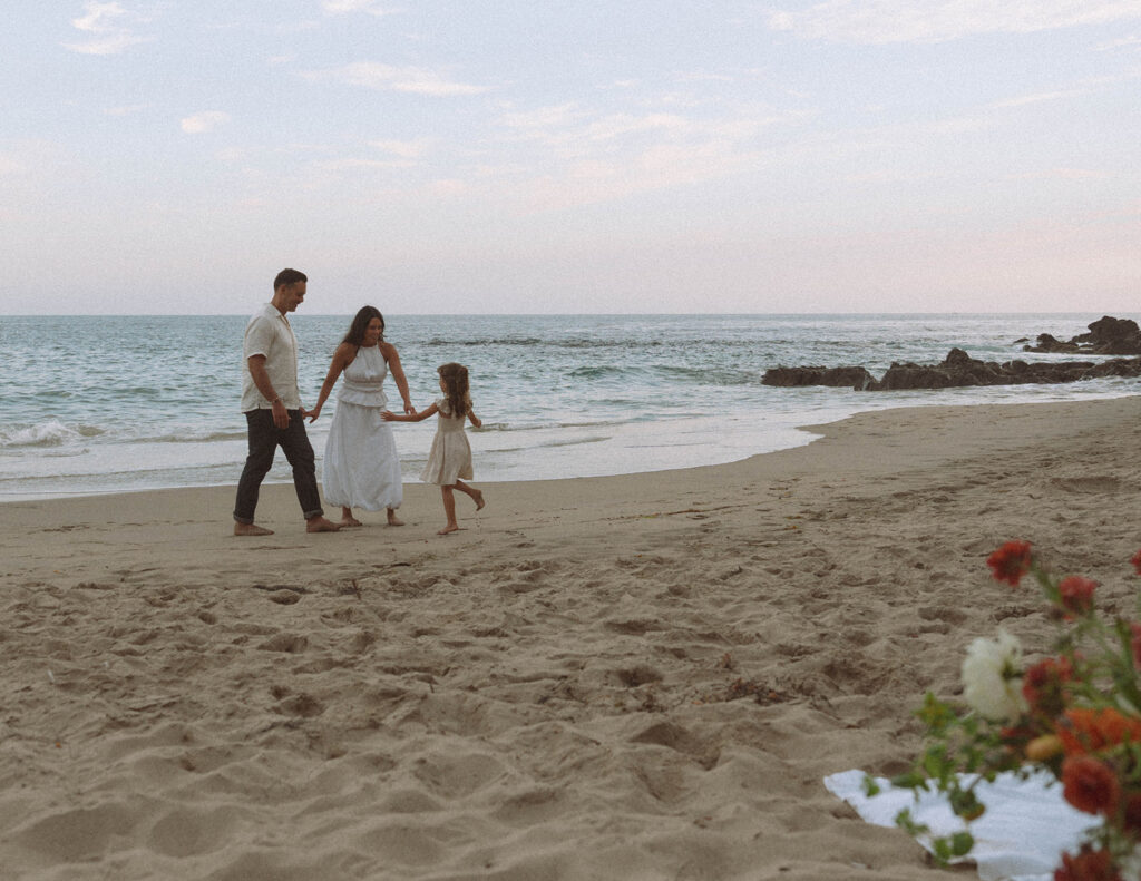 A wide view of a family walking along Crescent Bay at dusk, the beach and ocean stretching behind them with pastel evening light.