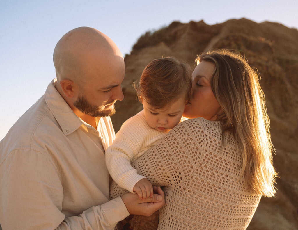 Parents embracing their toddler in the warm evening light at Laguna Beach, photographed family photographer Maria Alcantara.