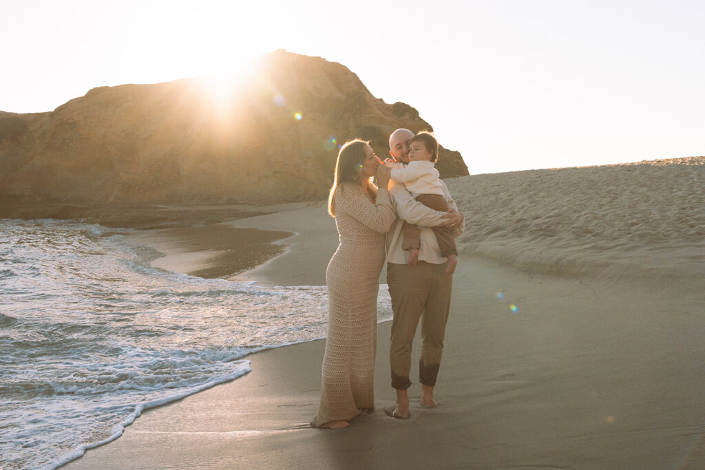 Family standing by the shoreline at Laguna Beach during golden hour, captured by family photographer Maria Alcantara.