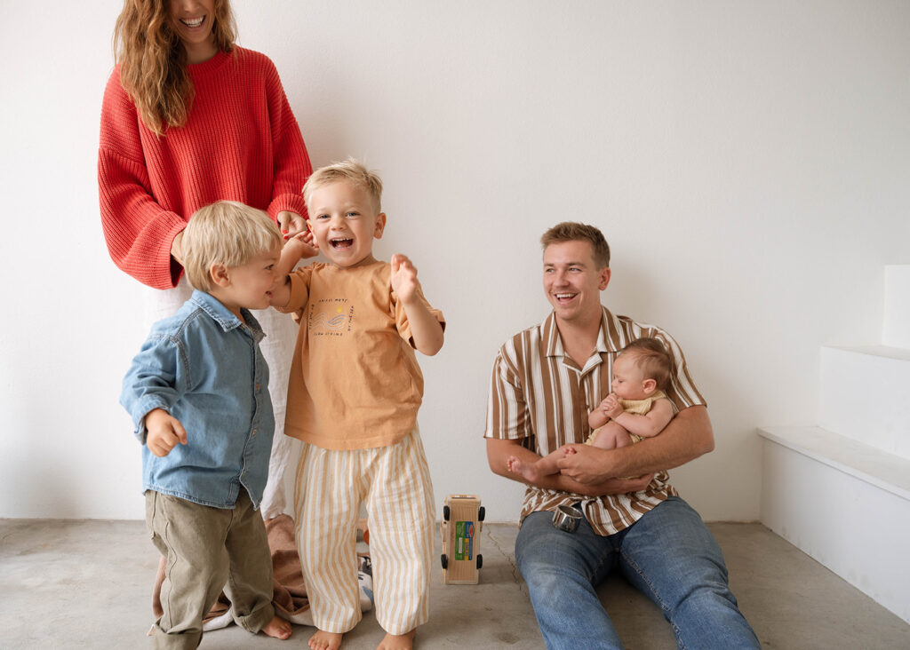 Family laughing together during a light-filled studio session, featuring natural connection and modern styling.