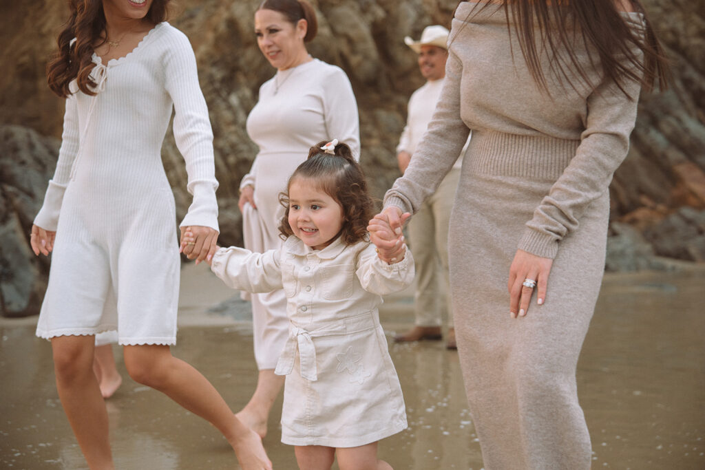 A little girl smiles while holding hands with her family as they walk across the sand at Crescent Bay in South Orange County.